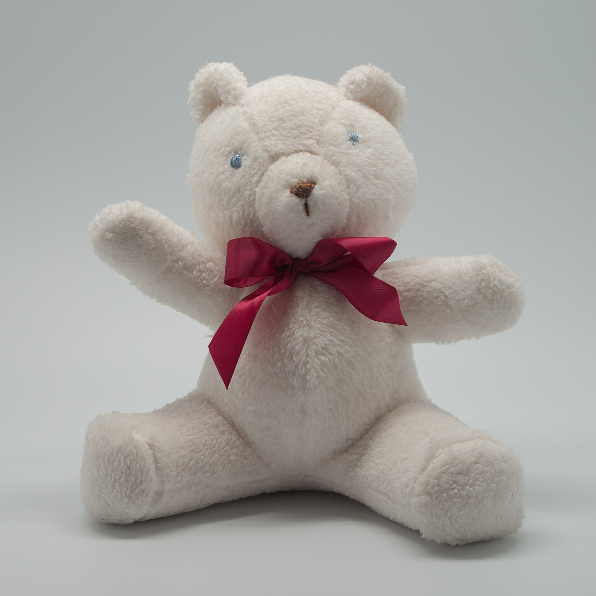 A handmade white teddy bear with a burgundy ribbon, representing personalized toy ideas